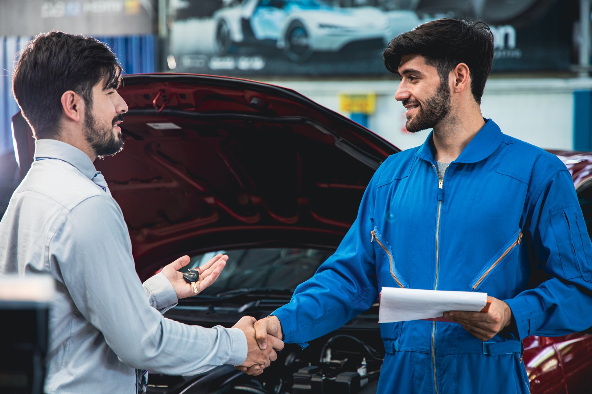 Man picking up car from garage a handsome male mechanic in a uniform returns the keys to the customer.